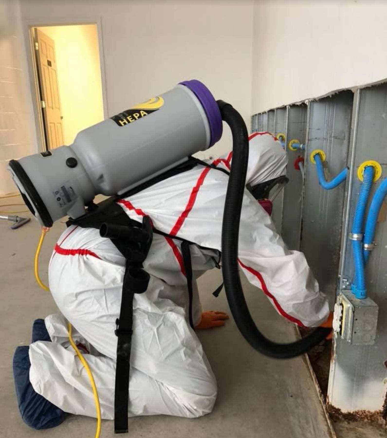 Technician with a backpack HEPA vacuum cleaning an opened wall cavity
