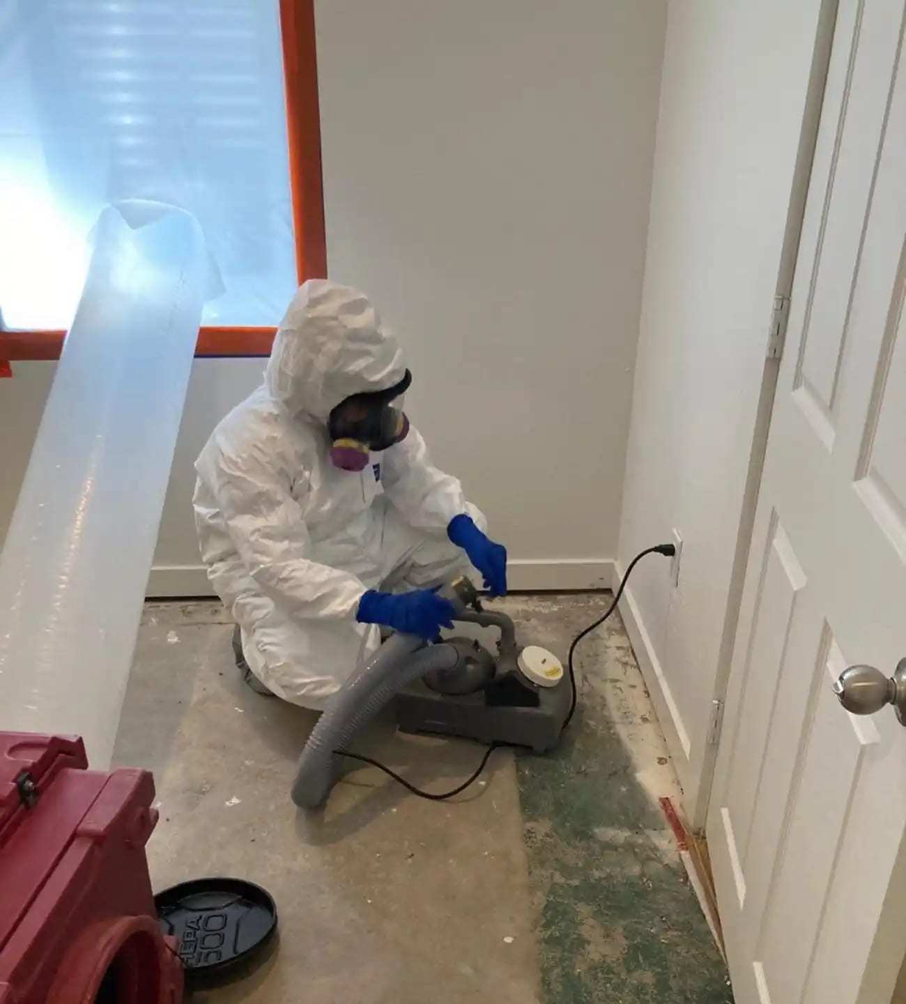 Technician in a protective suit and respirator cleaning the floor edge at a containment